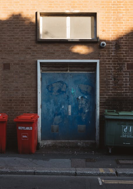 A large pile of waste and recycling bins situated on a paved area in front of a commercial building with a blue scaffolding structure and storefronts, including one labeled 'Cross Fish Bar.' The waste